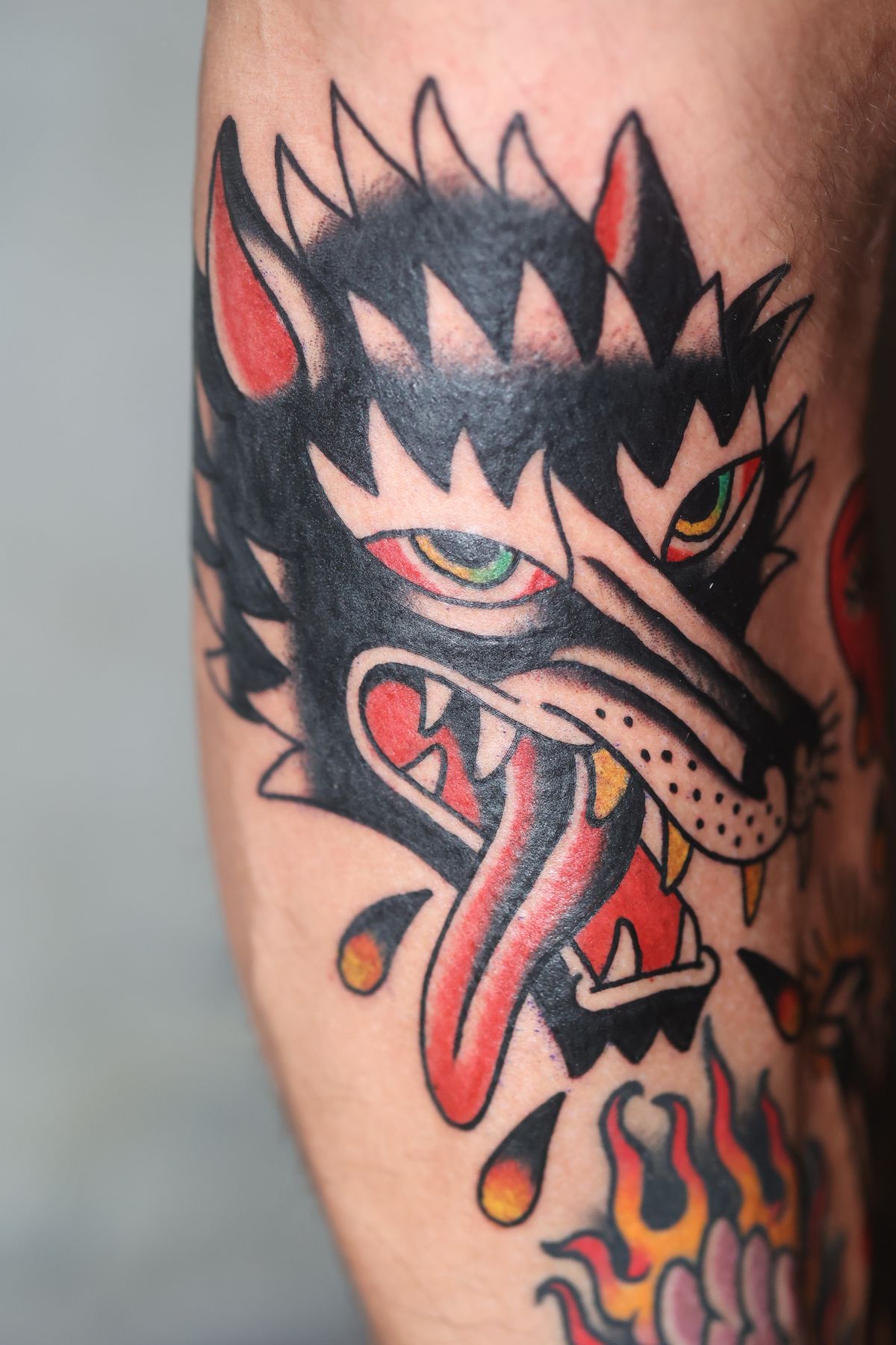 Black wolf head with tongue and flames, American traditional tattoo by Ulises Malavé