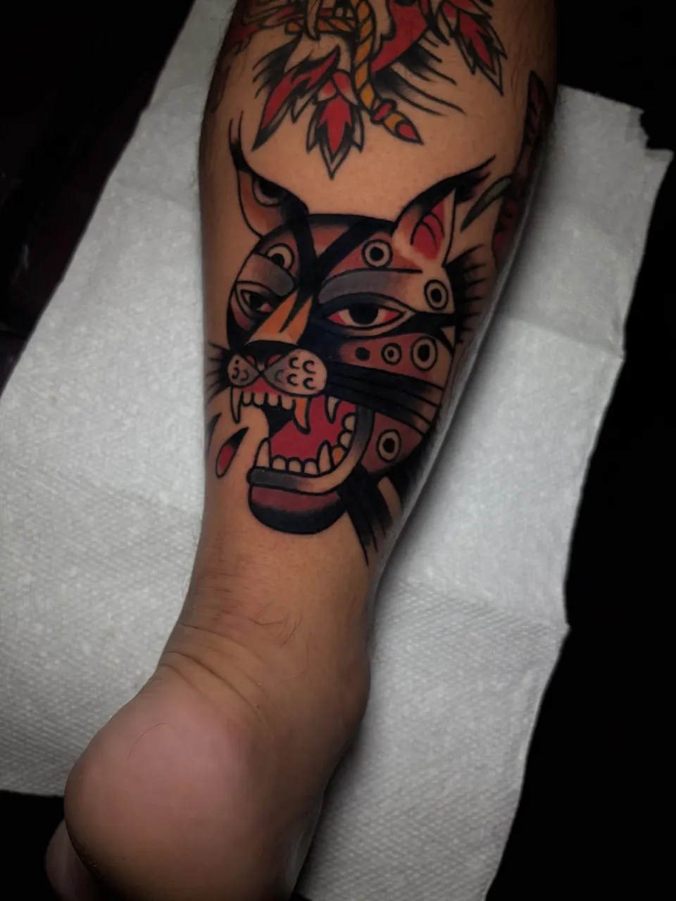 Cat head with ornamental eyes, color traditional tattoo on shin by Ulises Malavé